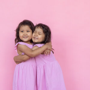 Maia and Jenna Schwartz, 9 year old twins on their birthday hug in front of pink background. Photo taken by JC photography studio.